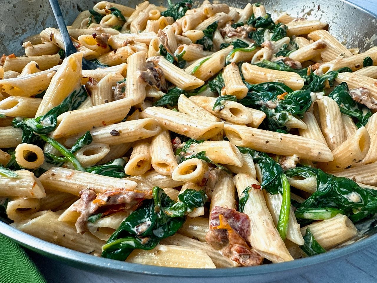 penne pasta, spinach, and sun dried tomatoes in a skillet 