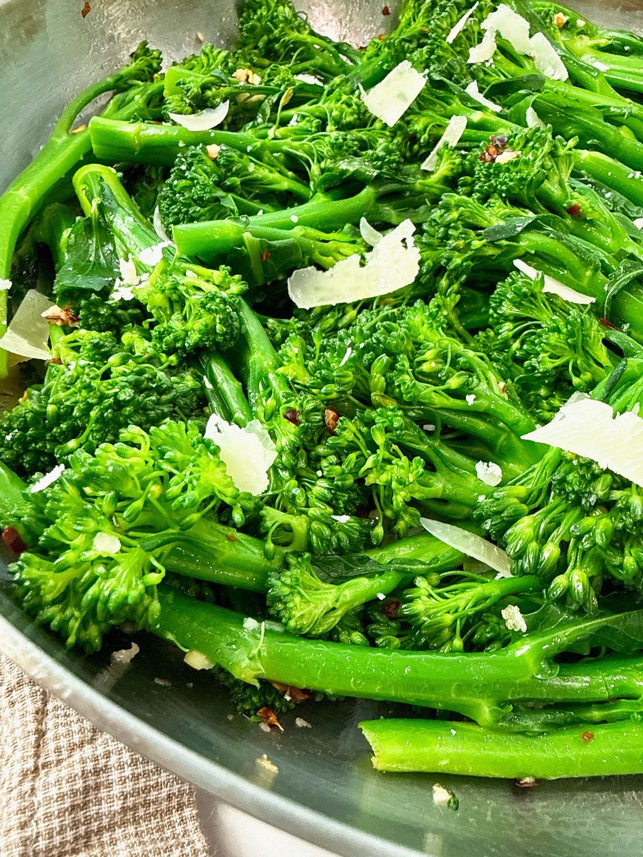 broccolini and pecorino romano in a silver skillet with black spoon and brown towel