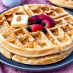 waffles on a grey plate with berries and butter