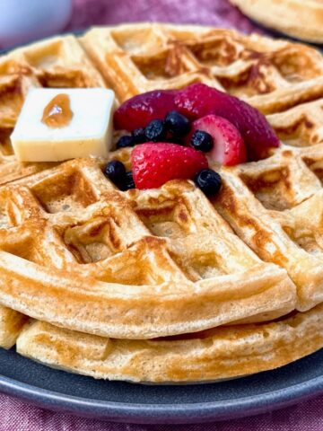waffles on a grey plate with berries and butter
