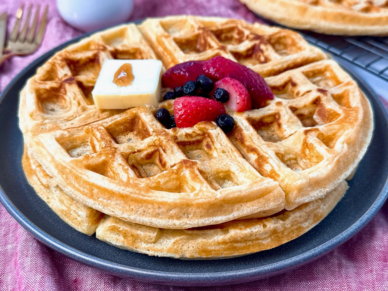 waffles on a grey plate with berries and butter