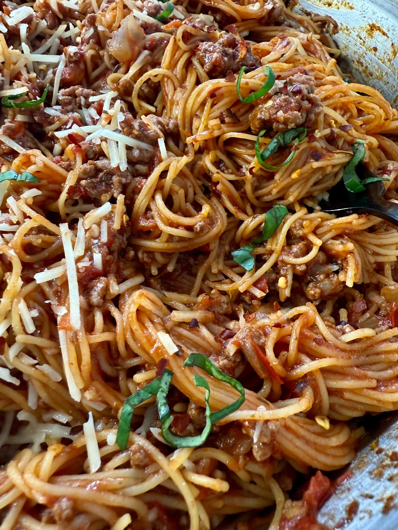 pasta bolognese in a silver pan with a black spoon