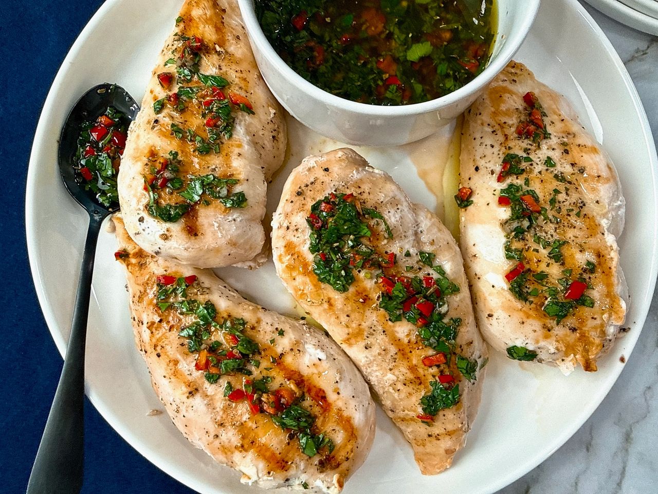 grilled chicken and bowl of chimichurri sauce on a white plate with a black spoon