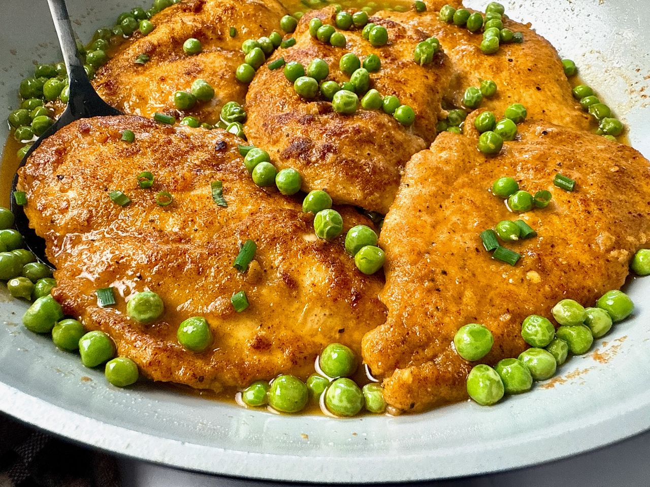 parmesan chicken and peas in wine sauce in white skillet