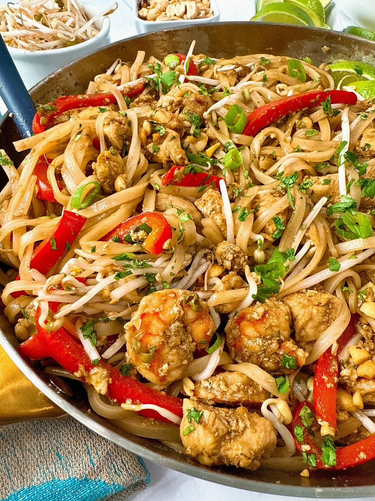 pad thai in a silver skillet with peanuts on the side