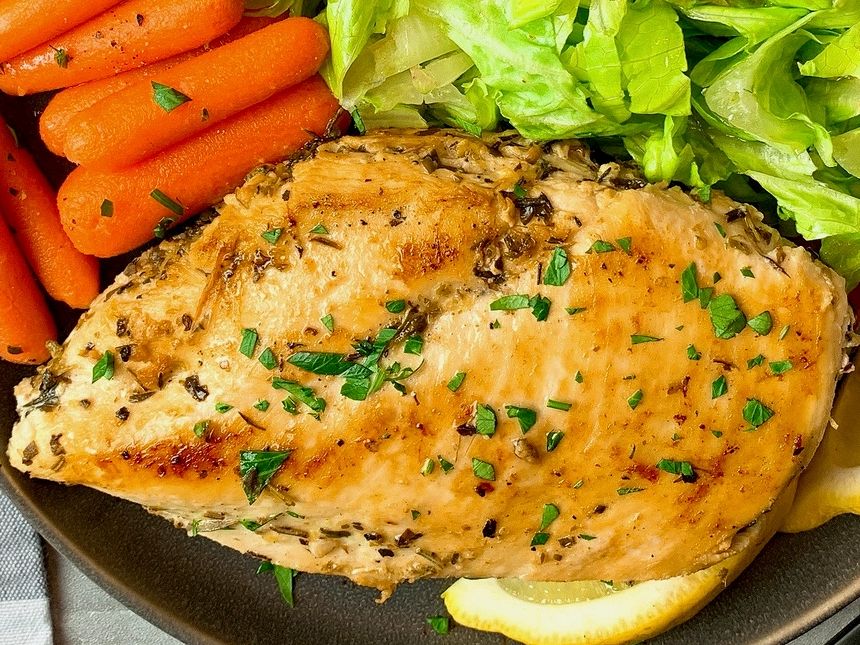 chicken breast on a plate with vegetables and lemon