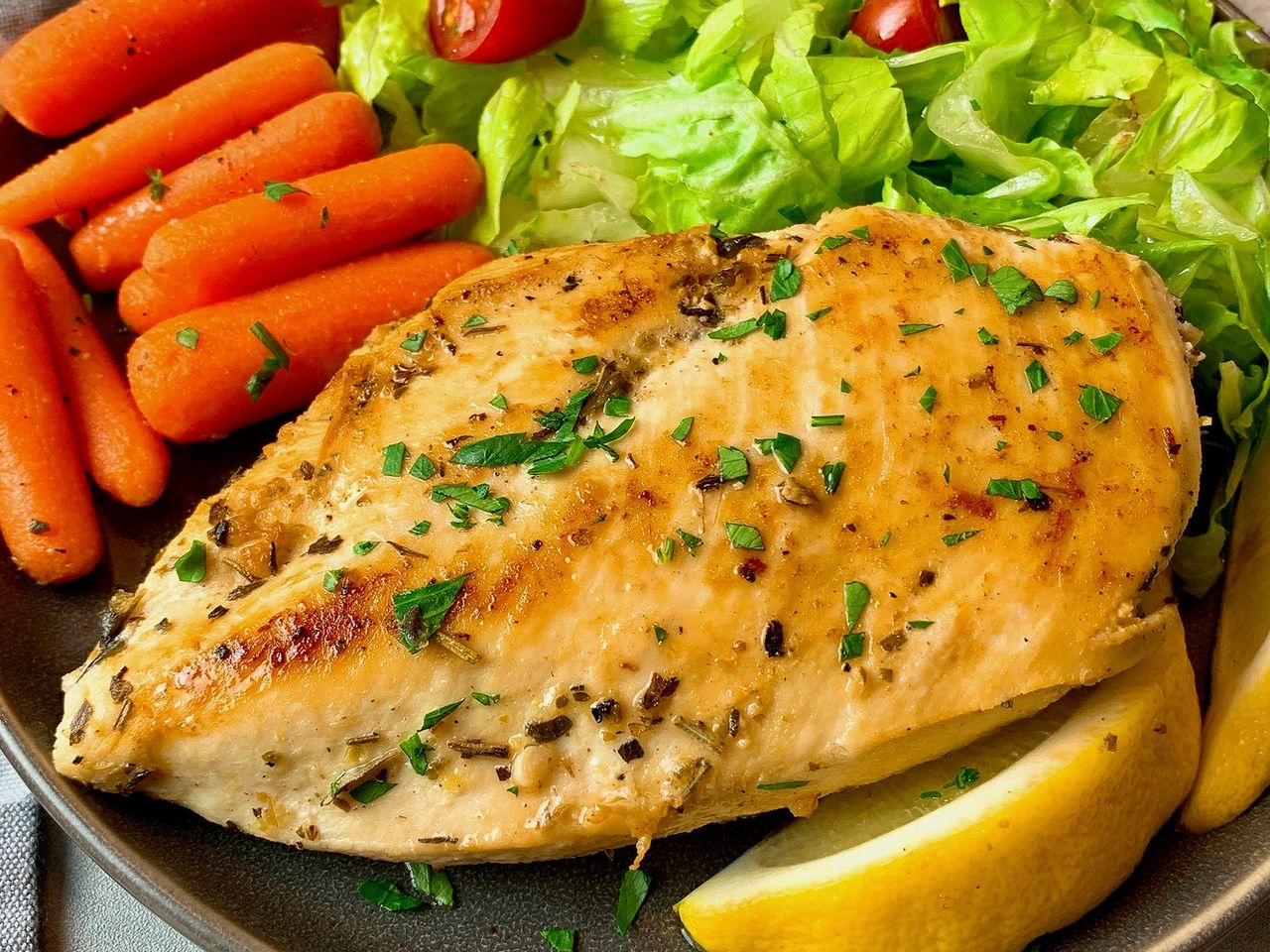chicken breast on a plate with vegetables and lemon