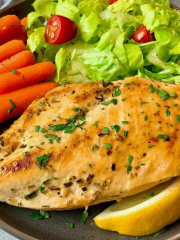chicken breast on a plate with vegetables and lemon